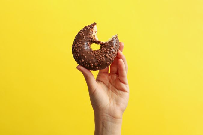 Female hand hold tasty donut on yellow background