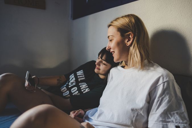 Happy lesbian couple using smartphone on bed