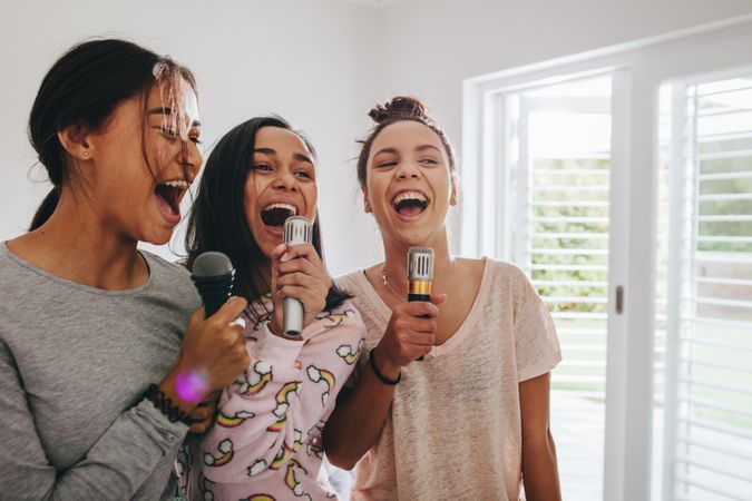 Group of young women singing holding microphones standing in bright bedroom