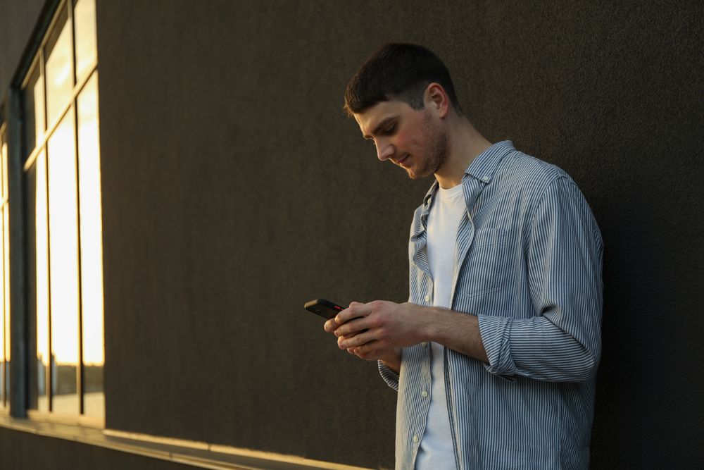 Young man uses a phone outdoor. Writing a message