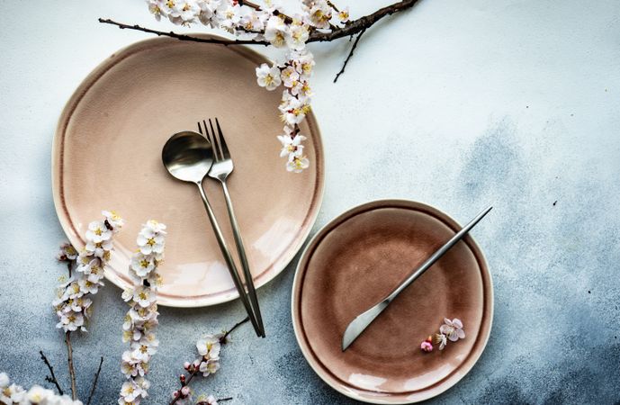 Top view of pink table setting of apricot blossom branches surrounding plates on grey counter