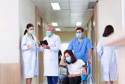 Male nurse pushing sick woman in wheelchair in busy hospital
