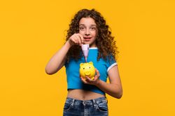 Surprised girl inserting 500 euro into piggy bank