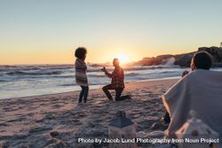 Young man kneeling and proposing woman with a ring at beach 5kNNj0