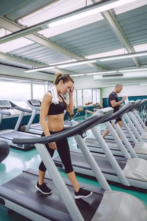 Man and woman doing cardio on treadmills in gym, vertical composition