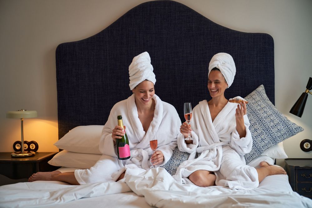 Happy women resting on bed with champagne and croissants