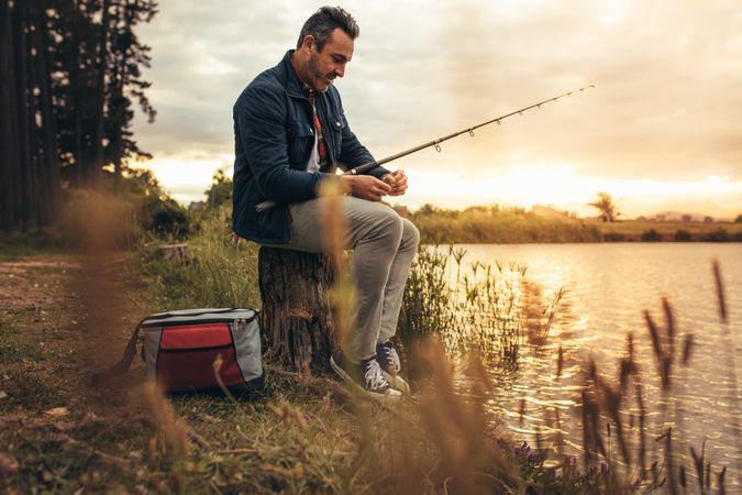 Man sitting on a tree trunk beside a lake with his fishing rod