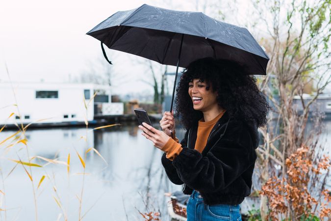Cheerful Black woman with smartphone and umbrella