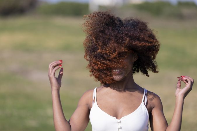 Female pictured outside in park with curly hair covering her face