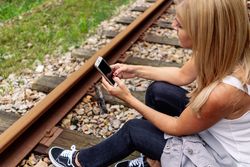 Cheerful woman sitting on railway with smartphone