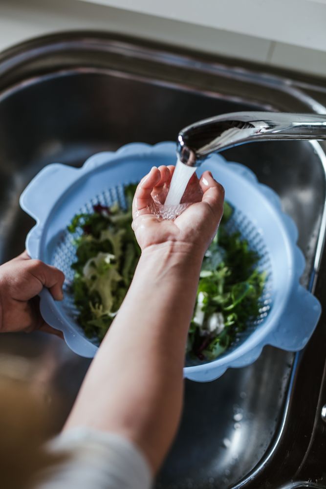 Crop child washing herbs for salad