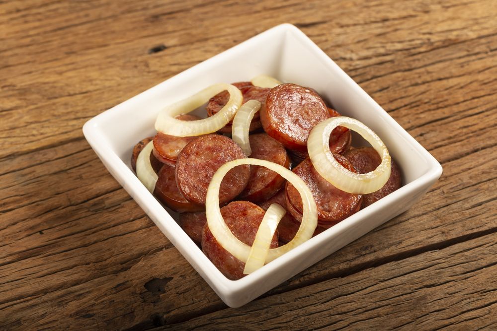 Sliced calabrese sausage with onion on wooden background.