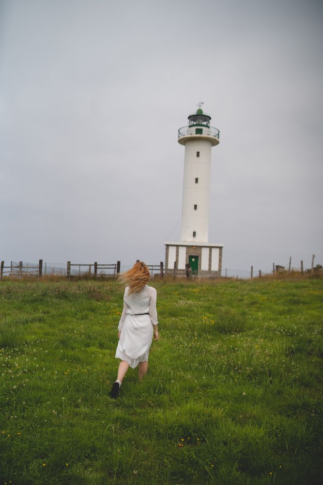 Woman walking in green meadow near lighthouse