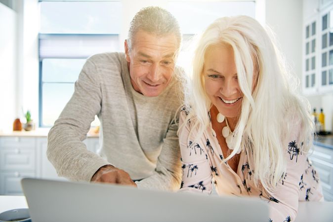 Mature couple smiling at a laptop screen in bright kitchen