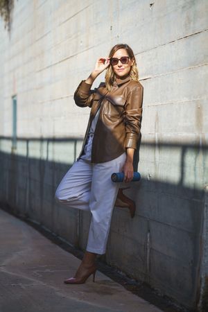 Woman with sunglasses leaning on wall carrying a thermos for coffee