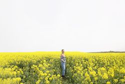Content woman in jeans in yellow field on overcast day