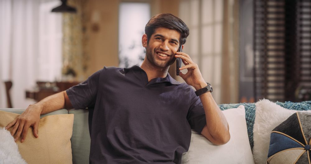 Young Indian Man Talking On The Phone At Home: Discussing Work Updates, Coordinating with Colleagues