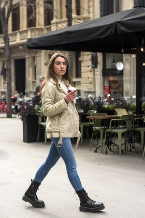Portrait of woman walking in a European city street, with to go coffee in hands