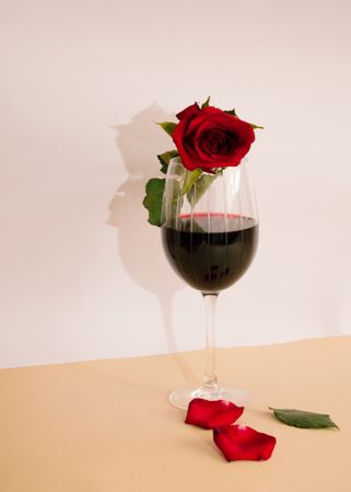 Glass of red wine with rose in it and fallen petals and leaf