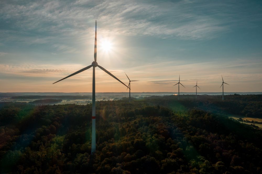 Drone shot with a multitude of wind turbines in the forest at sunrise in Germany