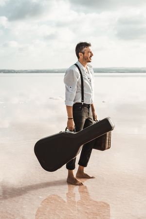 Focused stylish man with suitcase and guitar gig bag on seaside