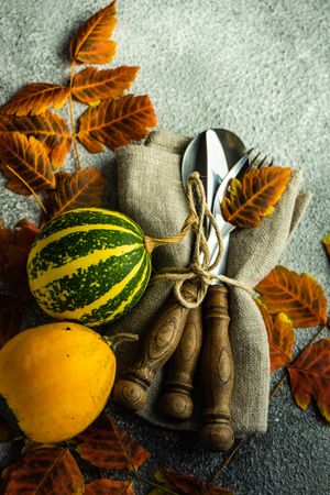 Fall table setting with orange yellow leaves and squash on stone background