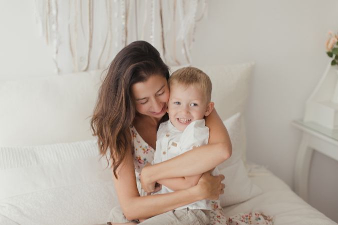 Mother ticking little son and laughing on bed