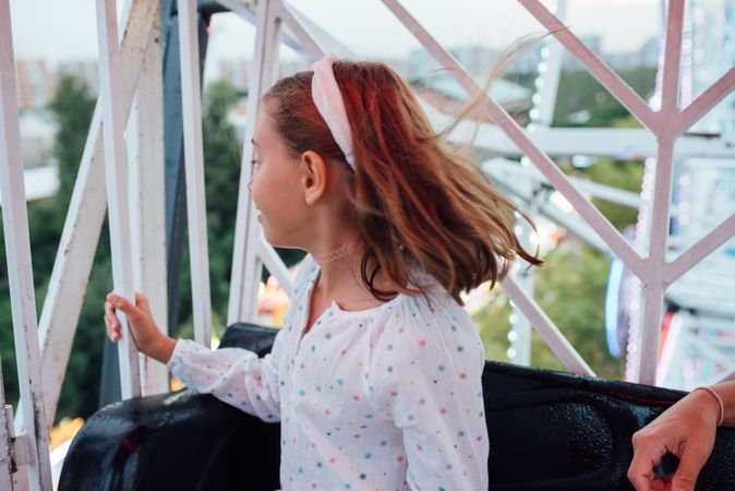 Cheerful girl riding Ferris wheel with parent