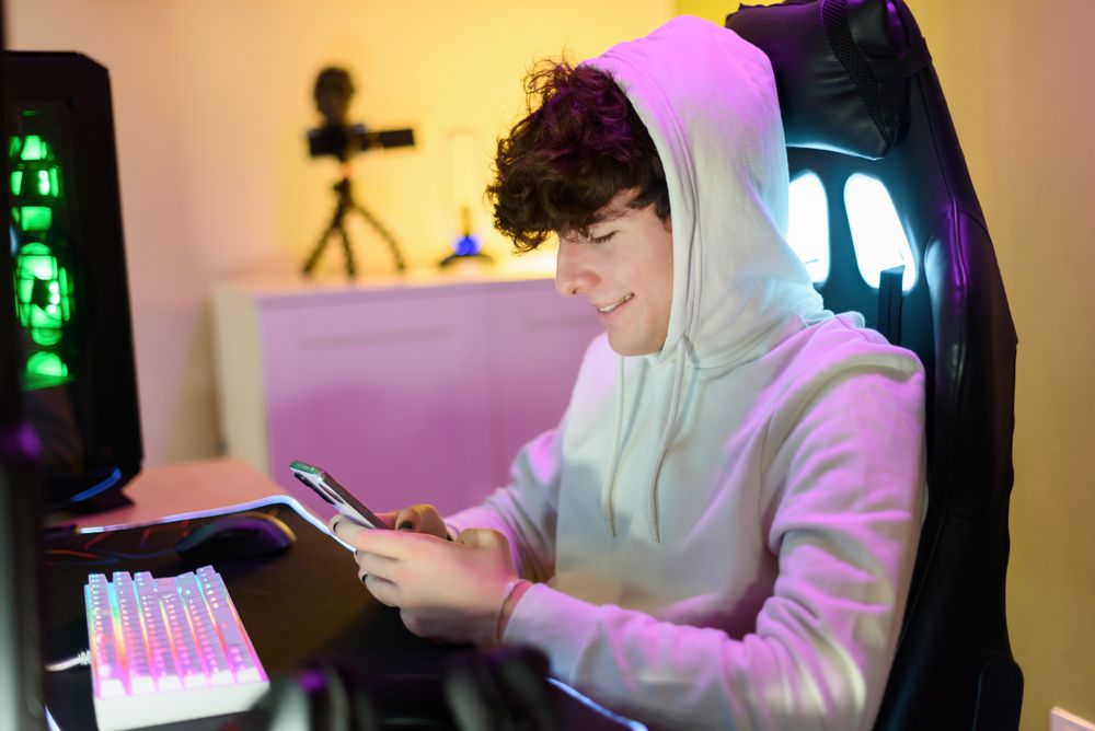 Focused happy young man sitting in chair and checking messages on smartphone