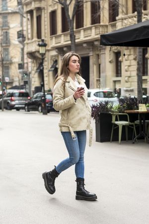 Portrait of woman walking in a city street, with takeaway coffee in hands