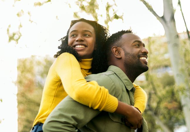 smiling Black man giving piggyback ride to happy woman