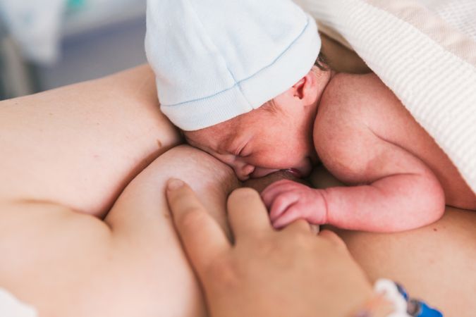 Close-up view of a woman breastfeeding her newborn baby in the hospital room after birth.