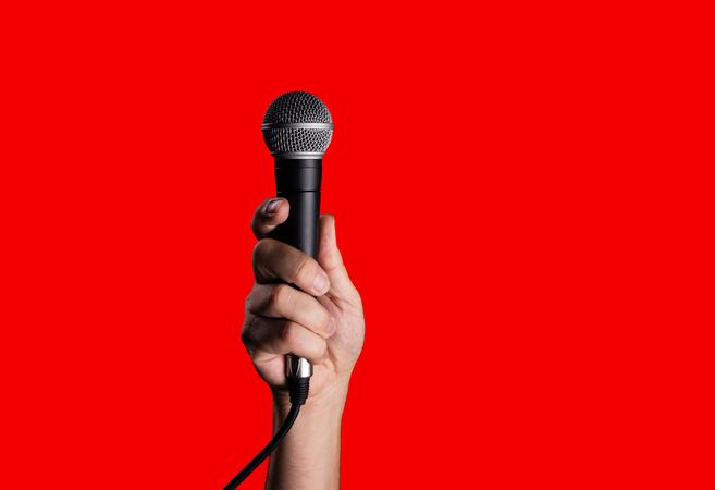 Hand holding a dynamic microphone on a solid red background.