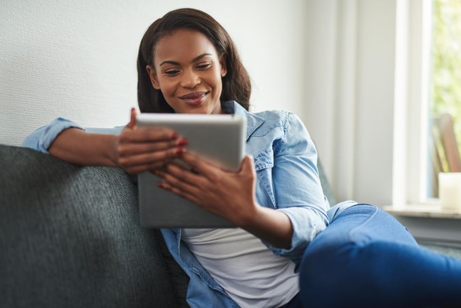 Woman smiling at tablet sitting on coach