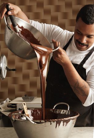 Man in apron pouring melted chocolate in kitchen