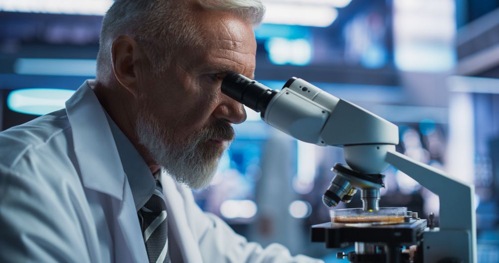 Medical Development Laboratory: Close Up Of Male Scientist Using Microscope, Analyzes Petri Dish Sample.