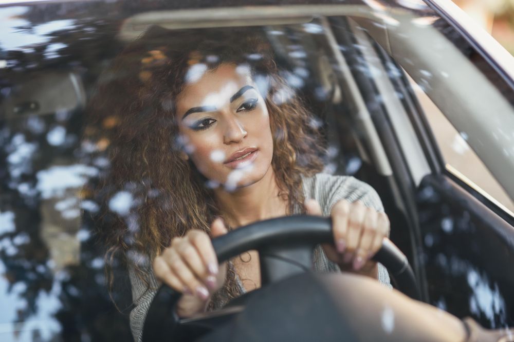 Serious female with curly hair sitting in car with hands on steering wheel