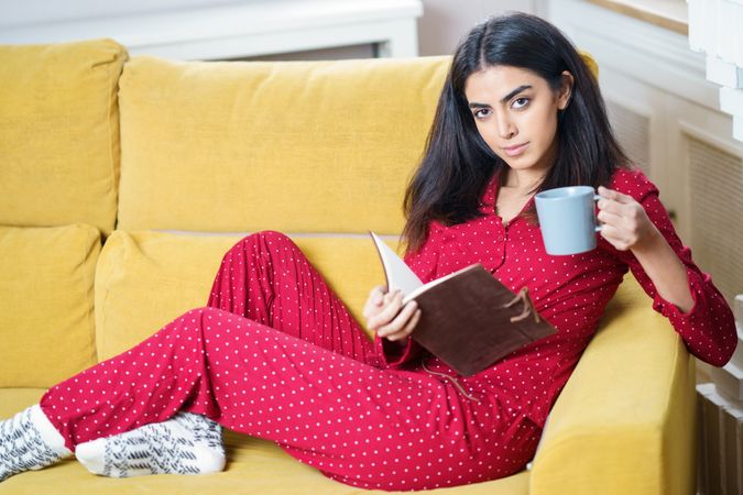 Woman relaxing in red pajamas at home with book