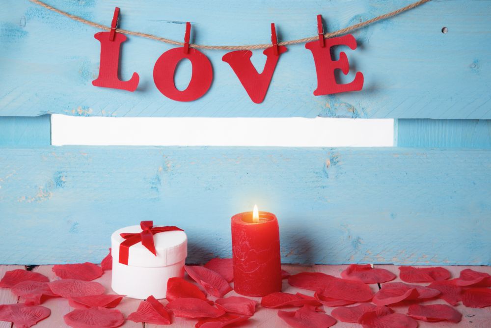 Gift box and the word love spelled out in paper letters hanging on twine with a candle in front