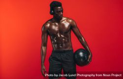 Shirtless man standing with medicine ball against red background 4dG2l5
