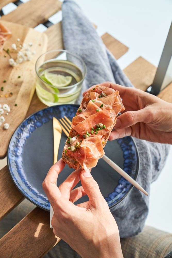 Crop anonymous lady eating yummy prosciutto toast during breakfast
