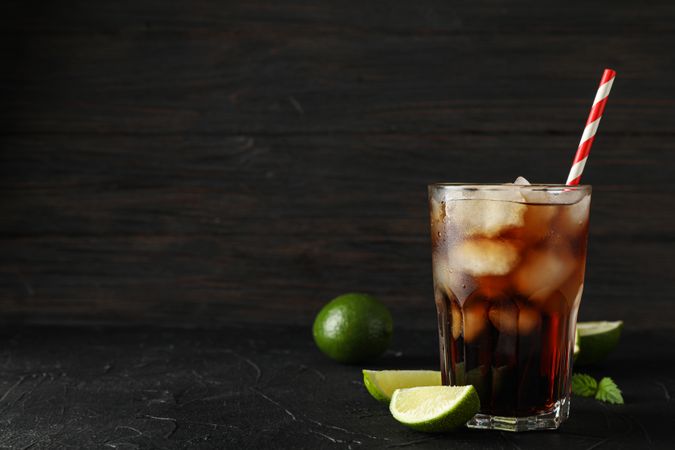 Glass of cold cola and limes on cement background