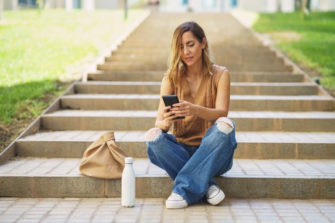 Stylish woman using smartphone sitting on street