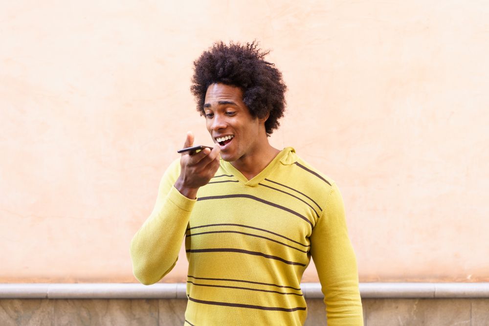 Man taking voice notes with his phone against peach wall