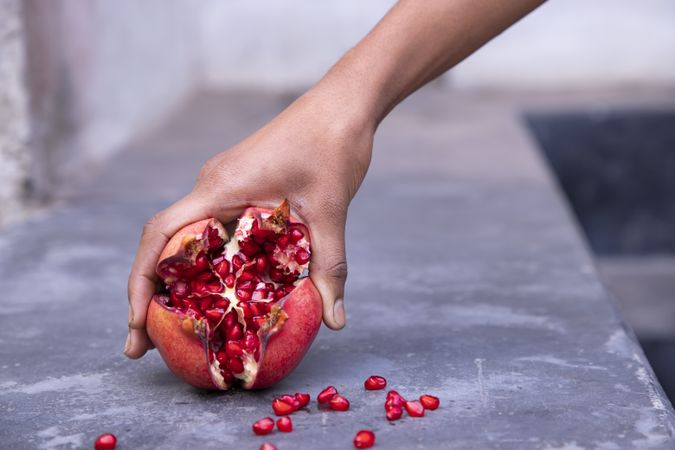 Hand holding pomegranate fruit in hand on stone background, close up