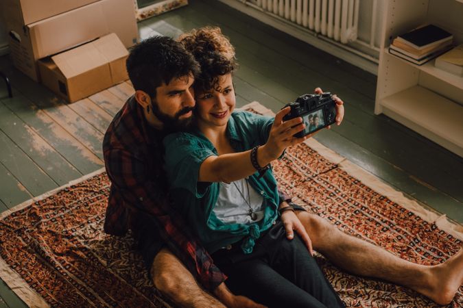 Joyful couple embracing and taking selfie on camera at home