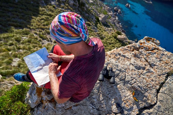 Unrecognizable hiker reading map on cliff