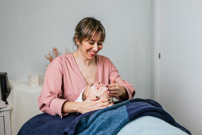 Crop beautician cleansing face of woman in salon