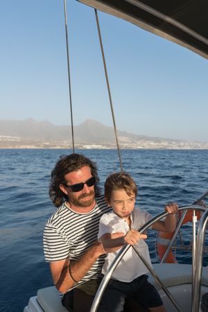Man with boy holding steering wheel on yacht on water