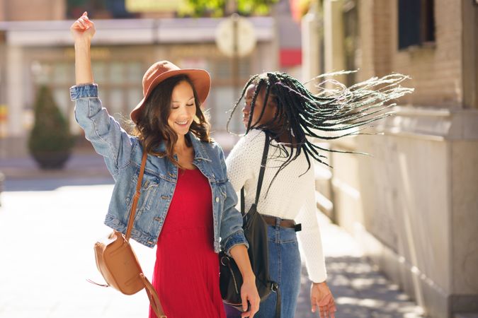 Female friends walking down a sunny street while dancing together